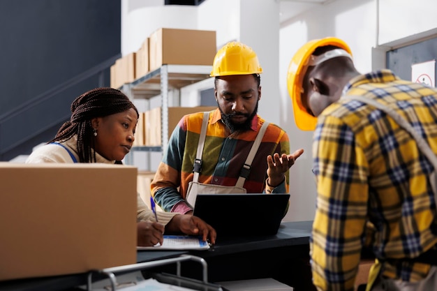 Free photo logistics department managers planning stock supply schedule at warehouse counter desk. all black storehouse employees team managing parcel registration and dispatching process