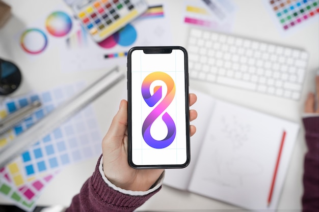 Foto gratuita designer di logo che tiene in mano uno smartphone con un bel logo su di esso