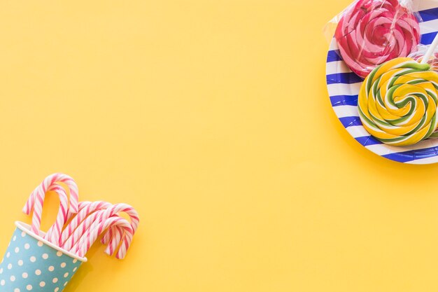 Lollipops candies and christmas candy canes in disposable cup on yellow background