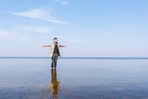 Free photo a lone young man outstretching his hand standing in the shallow sea water