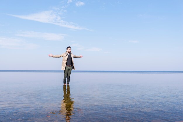 浅い海の水の中に彼の手の立っている広げて一人の若い男