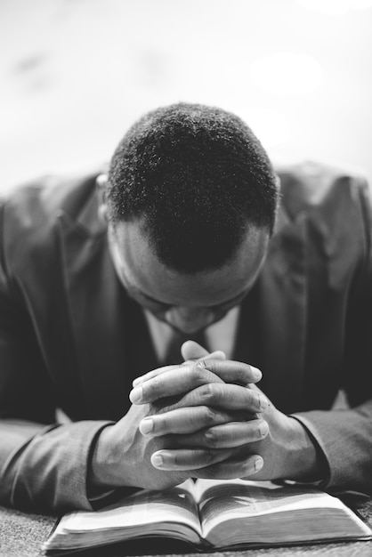 Foto gratuita un maschio africano-americano solo che prega con le sue mani sulla bibbia con la sua testa in giù