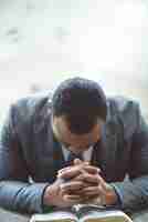 Free photo lonely african-american male praying with his hands on the bible with his head down