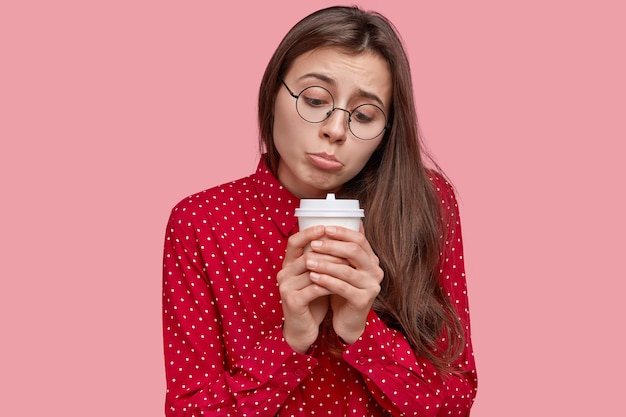 Lonely dejected woman purses lower lip, holds disposable cup of hot drink, feels sad, being in low spirit