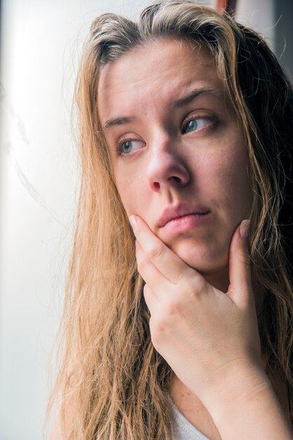 lonely girl near window thinking about something. Sad woman looking the rain falling through a window at home