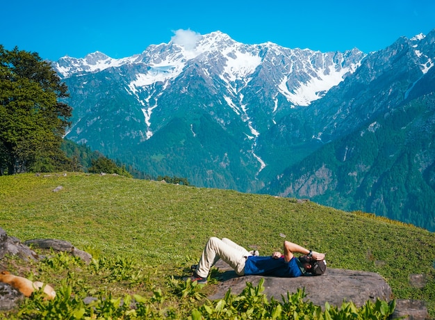 山のある牧草地で横になって日光浴をしている孤独な男性
