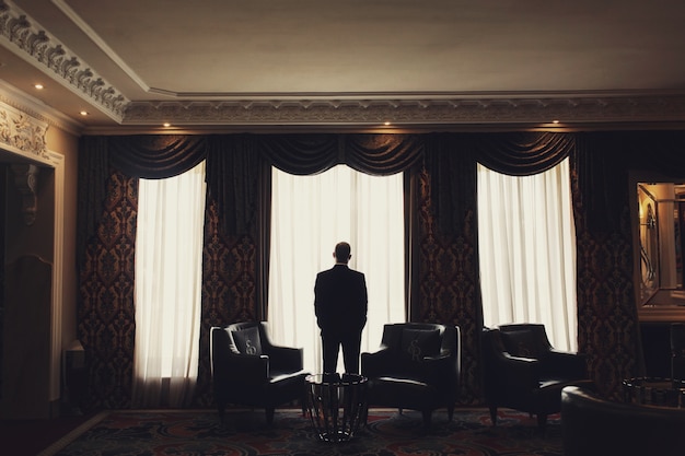 Одинокий мужчина стоит перед окном в комнате