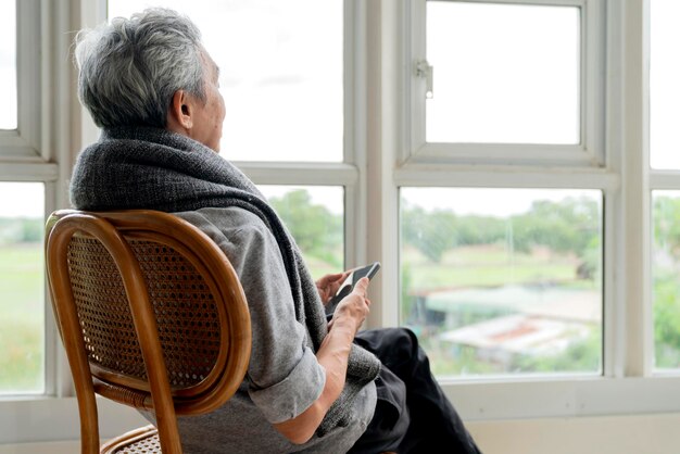孤独な年配の男性男性が自宅の窓の外を窓から眺めるのを楽しんでいるリビングルームに座っている慢性疾患アルツハイマー病の年配の男性の側面図