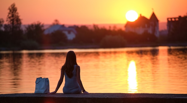 暖かい​夜​に​湖岸​に​一​人​で​座っている​孤独な​女性​。​自然​の​概念​の​孤独​と​リラックス​。