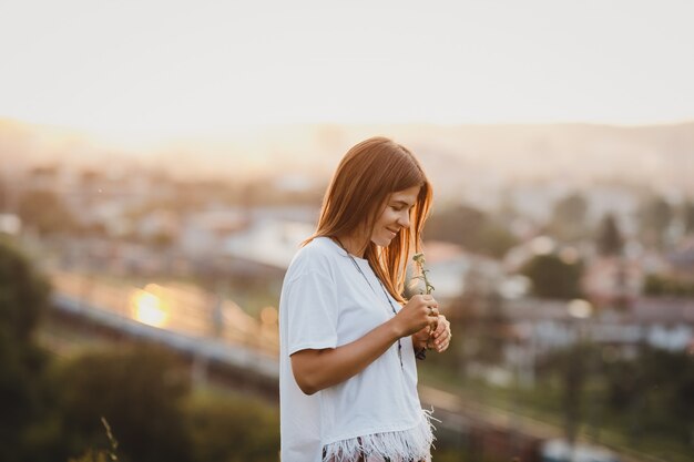 Lonely woman in white shirt stands with a field flower 