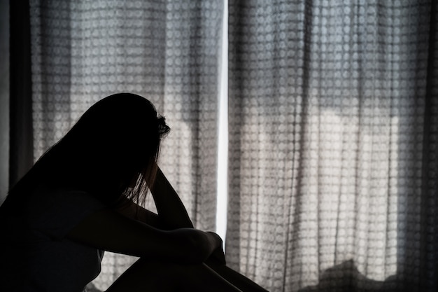 외로운 젊은 여자가 우울하고 어두운 침실에 앉아 스트레스, 부정적인 감정 개념