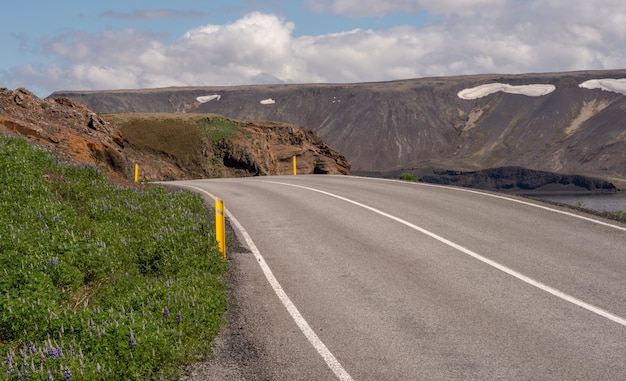 Long asphalt road surrounded by high mountains under the cloudy sky