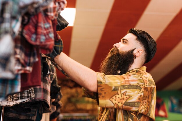 Long bearded man looking at clothes hanging on the rail in shop