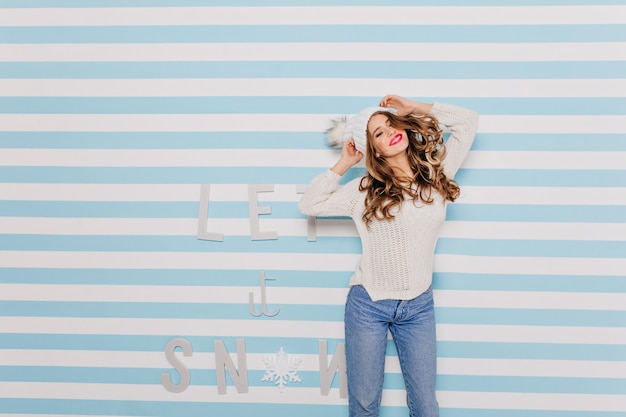 Long curls of Slavic girl fly away beautifully because of rhythmic dance movements. Portrait of model in good mood in winter clothes