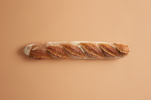 Long French baguette with crispy golden crust isolated on beige studio background. Freshly baked type of bread for tasty nutrition. Overhead shot. Tasty gourmet product baked on bakery. Food concept