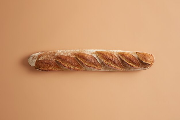 Long French baguette with crispy golden crust isolated on beige studio background. Freshly baked type of bread for tasty nutrition. Overhead shot. Tasty gourmet product baked on bakery. Food concept