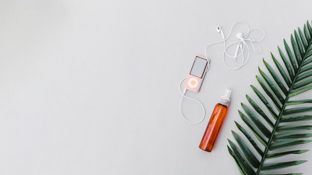 Long green leaf, perfume bottle and mp3 player with earphone on gray backdrop