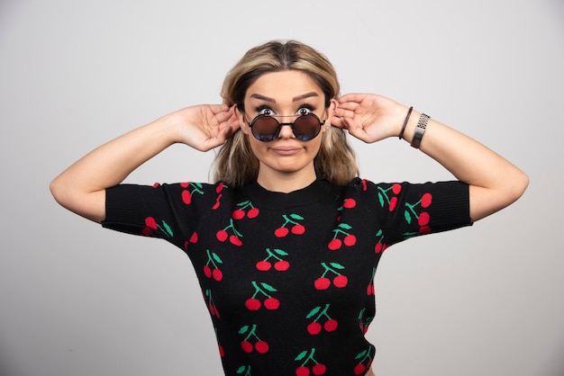 Long haired blonde woman in sun glasses standing on gray wall. 