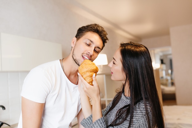 Long-haired european lady feeding bearded boyfriend with croissant