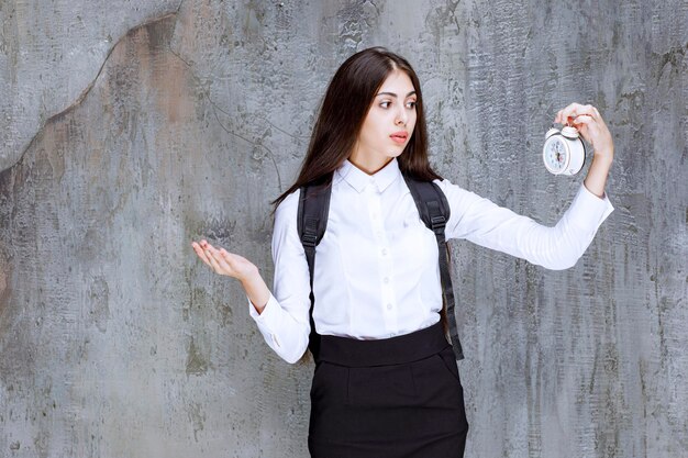 Long haired female student holding alarm clock, shocked about time. High quality photo