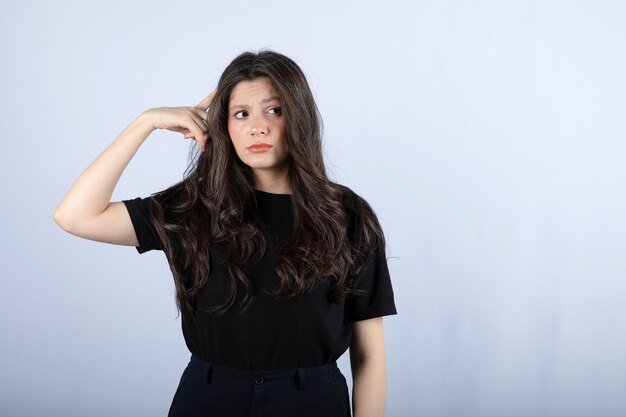 long haired girl standing and thinking on white wall. 