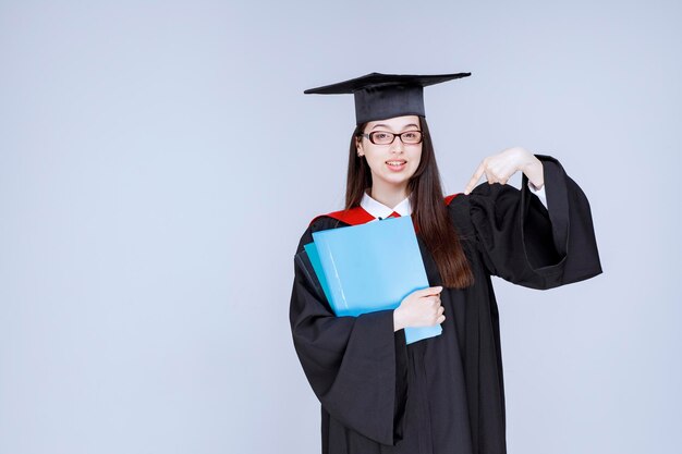Long haired student in glasses pointing at blue folders. High quality photo