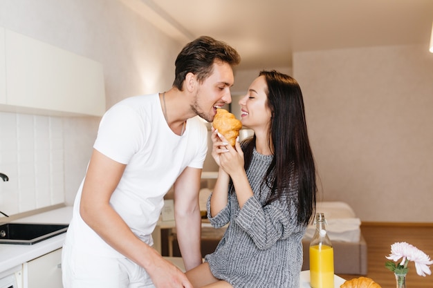 Long-haired woman feeding boyfriend with croissant and smiling