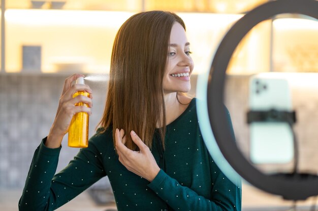 Длинноволосая женщина распыляет лак для волос на волосы и улыбается