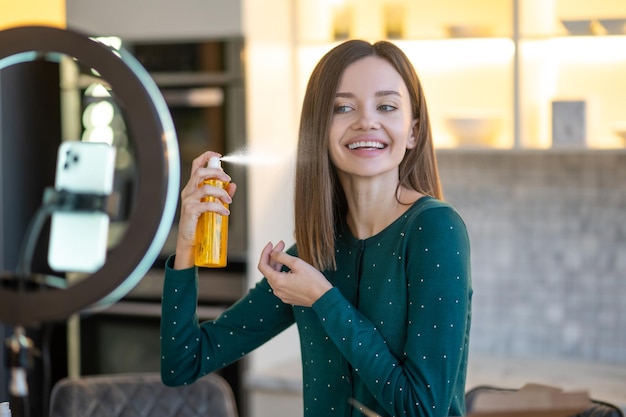 Free photo long-haired woman spraying hairspray on her hair and smiling