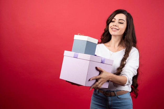 赤い背景にプレゼント ボックスに立っている長い髪の女性。高品質の写真