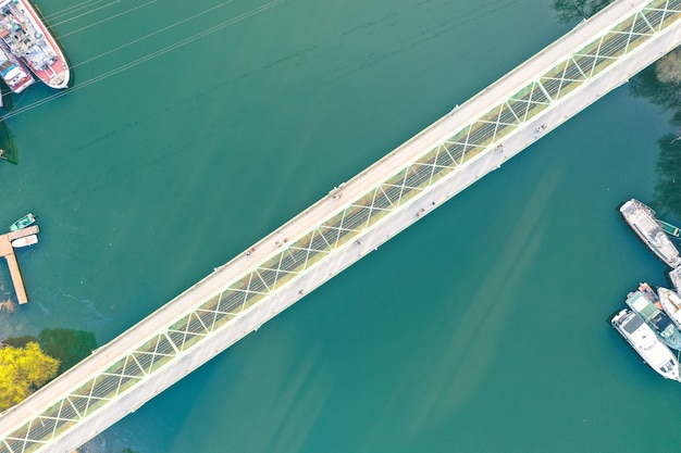 Long narrow bridge going over a large river with ships docked at the coast