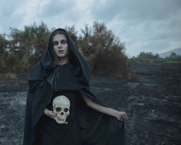 Long portrait of a man dressed as dark witch with skull