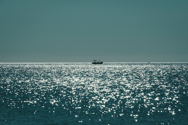 Long range shot of a boat sailing on the sea reflecting the sun