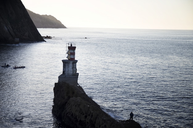 Long-range shot of a lighthouse on a cliff in the sea with people beside it