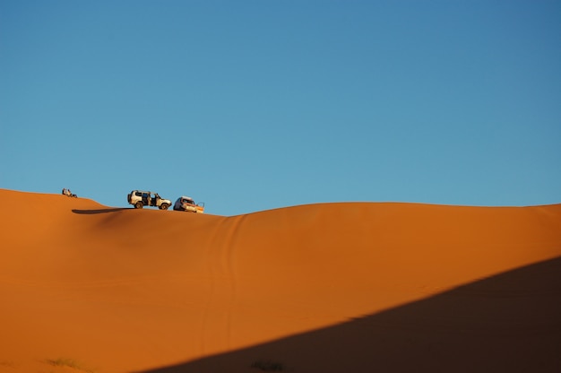Long-range shot of two cars parked on top of the sand dunes with clear blue sky on a sunny day