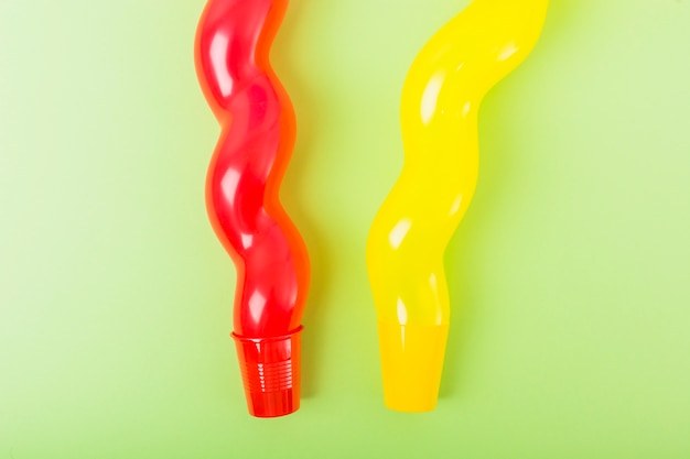Длинные красный и желтый воздушный шар над пластиковой чашкой на зеленом фоне