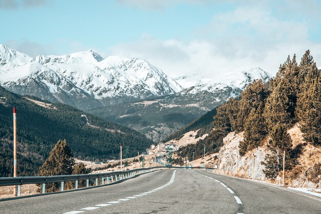 Long road surrounded by high mountains with tops covered in snow