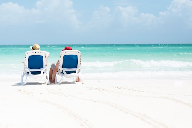 Foto gratuita vista lungamente indietro delle coppie che si siedono sulle sedie di spiaggia