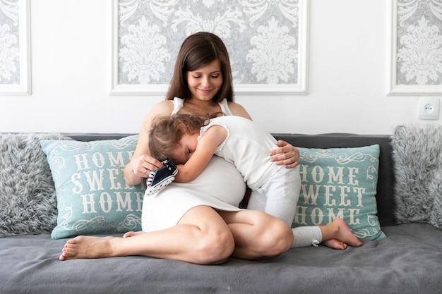 Long shot daughter hugging her mom on the sofa