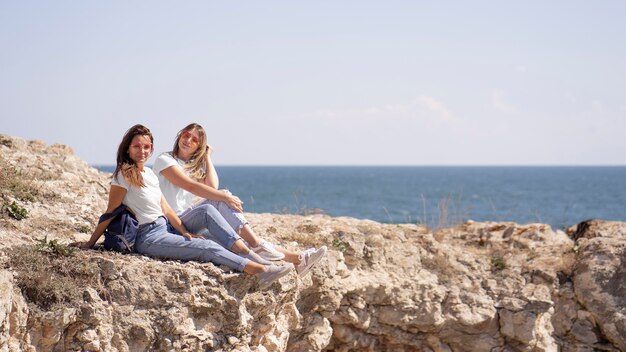 Long shot friends sitting on rocks next to the ocean with copy space