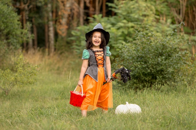 自然の中で魔女のハロウィーンの衣装を持つ少女のロングショット