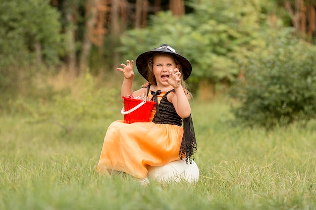 自然の中で魔女のハロウィーンの衣装を持つ少女のロングショット