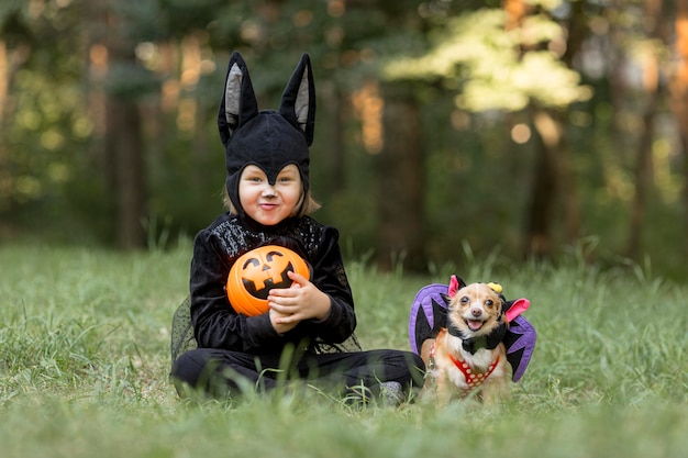 Colpo lungo del ragazzino in costume da pipistrello e cane