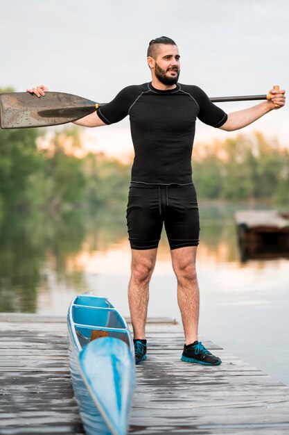 Long shot man posing with oar