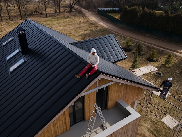 屋根の上に座っているヘルメットを持つロングショットの男