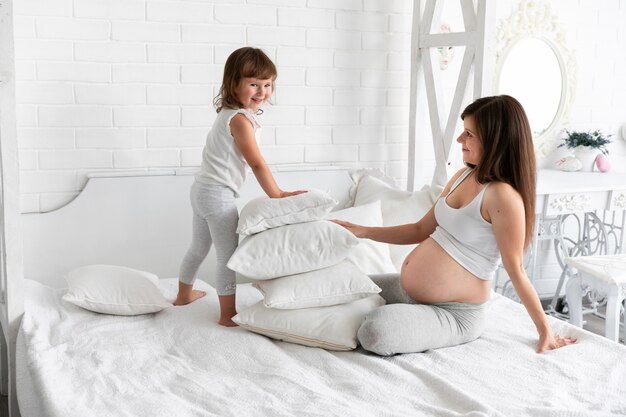 Long shot mother and little girl playing with pillows 