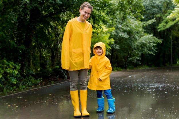 Free photo long shot mother and son holding hands while raining