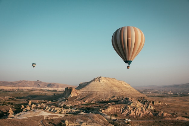 Long shot of multi-colored hot air balloons floating above the mountains