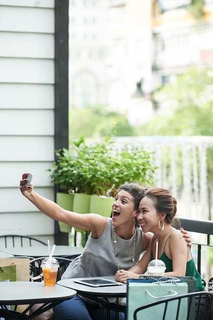 無料写真 夏のカフェで面白いselfieを取っている2人の女の子のロングショット