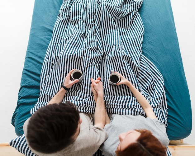 Long shot of people sitting in bed drinking coffee